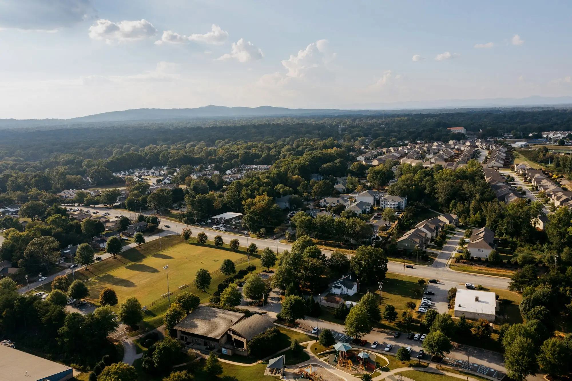 Aerial view of a residential neighborhood with tree-lined streets, a park, and hills on the horizon